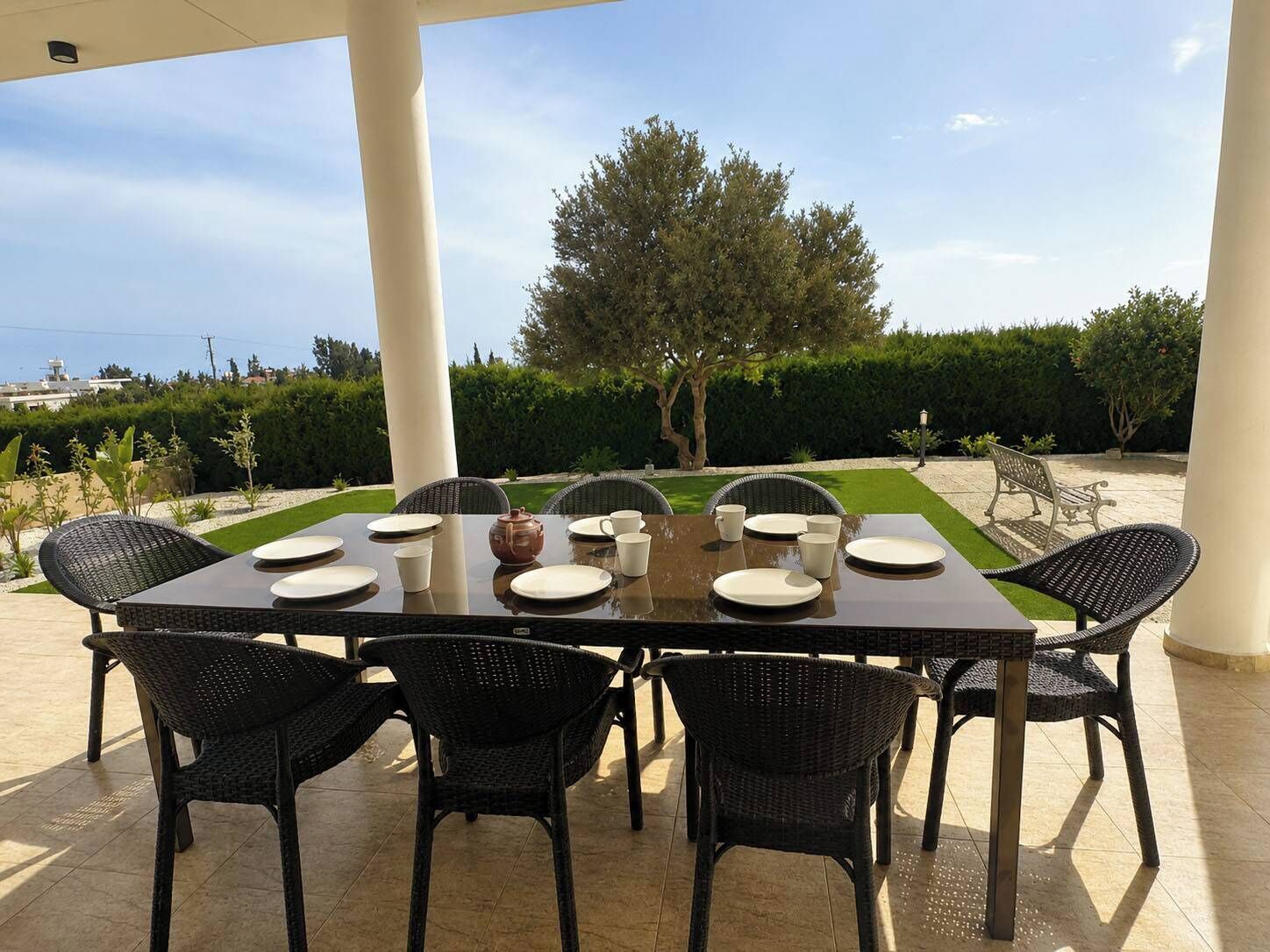 An outdoor dining area with a table set for six, surrounded by wicker chairs, under a covered patio.