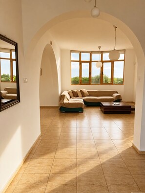 A spacious living room with a large sectional sofa, a coffee table, and a view of greenery through large windows. - Luxury, Modern Villa with private pool & garden in Coral Bay area (Πέγεια, Πάφος)