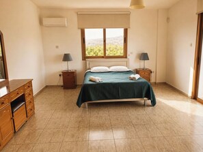 Ein Schlafzimmer mit einem Bett, zwei Nachttischen, einem Schminktisch und einem Fenster mit Aussicht. Eine Klimaanlage ist ebenfalls vorhanden.