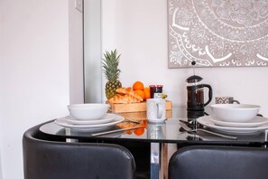 A dining table with two white bowls, a glass pitcher, a jar of jam, a pineapple, oranges, and a croissant on a wooden board. - Bedford Road Garden Apartment (Bedford)