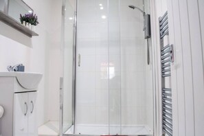 A modern bathroom with a glass-enclosed shower, a white sink, and a towel rack. - Bedford Road Garden Apartment (Bedford)