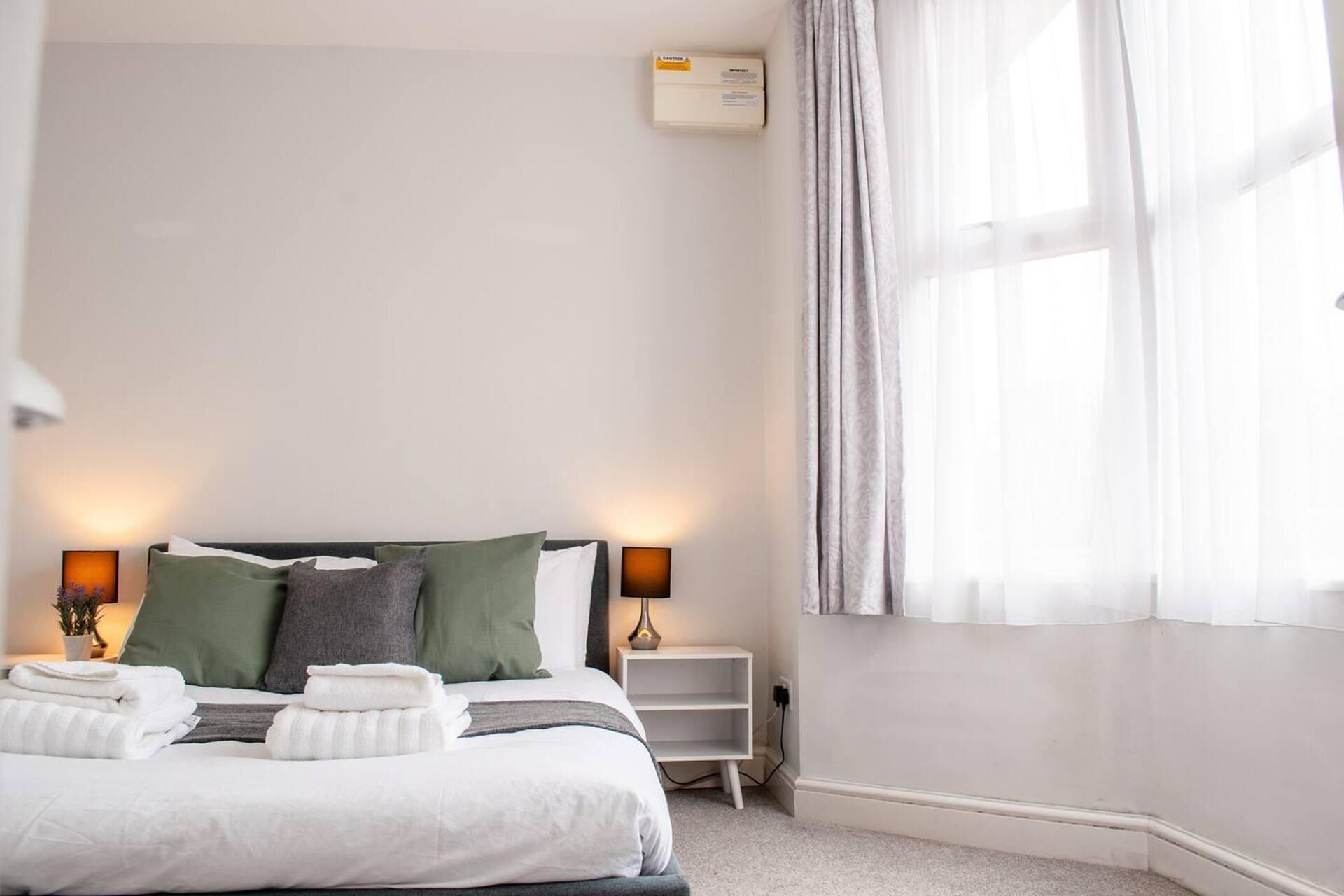 A neatly made bed with pillows, a bedside lamp, and a small white nightstand with a lamp.