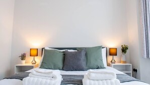 A neatly made bed with two pillows, two bedside lamps, and two towels. - Bedford Road Garden Apartment (Bedford)