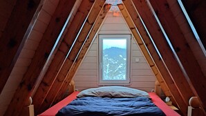 Una habitación pequeña con techo inclinado, una cama individual, un ventanal y un aparador.