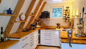 Una cocina con vigas de madera, microondas, pileta y diferentes utensilios de cocina.