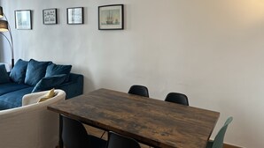 Een kamer met een houten tafel, vier stoelen, een blauwe bank met kussens en vier ingelijste foto's aan de muur.