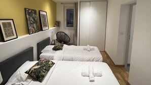 Een hotelkamer met twee bedden, een geel accentmuur, ingelijste foto's, een stoel en een deur die naar een andere kamer leidt.