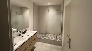 Een moderne badkamer met een grote spiegel, twee wastafels, een douche en een betegelde vloer.