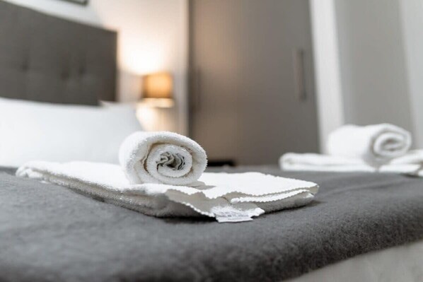 A neatly made bed with white towels and a grey blanket.
