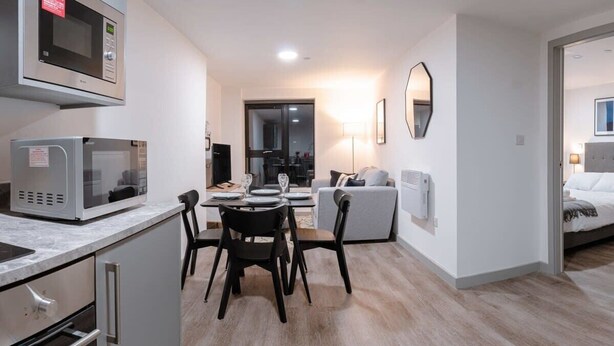 A modern kitchen with a microwave, a dining table with chairs, and a sofa in the living area. - Contemporary 1 Bed Apartment in Central Liverpool (Liverpool)