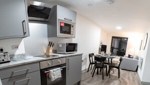 A modern kitchen with stainless steel appliances, a dining area with a table and chairs, and a grey sofa in the living area. - Contemporary 1 Bed Apartment in Central Liverpool (Liverpool)