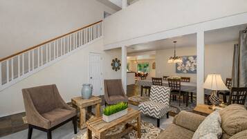 A spacious living room with a staircase, a dining area, and a kitchen in the background.