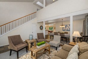 Un vaste salon avec un escalier, un coin repas et une cuisine à l’arrière-plan.