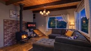 A cozy living room with a brick fireplace, a sofa, a television displaying 'NETFLIX', and a window with curtains.