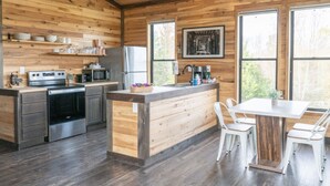 A modern kitchen with wooden walls, a central island, and a dining area with white chairs.