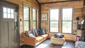 A cozy cabin interior with a brown leather sofa, a woven ottoman, and a bookshelf.