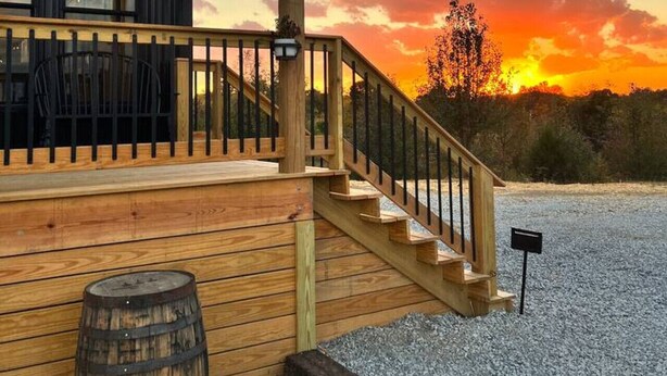 A wooden deck with a railing, a wooden barrel, and a sunset in the background.