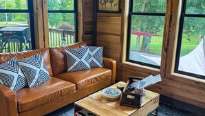 A wooden cabin interior with a leather sofa, a coffee table, and large windows. - Bourbon Barrel Cottages #3 on Ky. Bourbon Trail (Lawrenceburg)