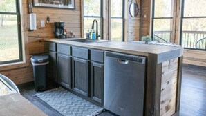 A kitchen with wooden cabinetry, a built-in dishwasher, a sink, and a window overlooking a deck. - Bourbon Barrel Cottages #3 on Ky. Bourbon Trail (Lawrenceburg)