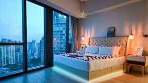 Ein Schlafzimmer mit großem Fenster, einem Bett mit Rosenblättern, einem Kronleuchter und Blick auf die Stadt.