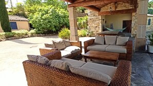 An outdoor seating area with wicker furniture and cushions, a hammock, and a stone building in the background. - Le Mas du Colombier - Les Vans - Ardèche Méridionale (Les Vans)