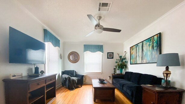 A living room with hardwood flooring, a ceiling fan, a dark blue sofa, a coffee table, and a TV on the left wall. - Rose District Bungalow pet friendly (Broken Arrow)
