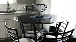 A kitchen with a round table and four chairs, a black metal chandelier, and a window with blinds. - Rose District Bungalow pet friendly (Broken Arrow)