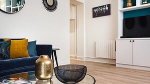 Una sala de estar moderna con un sofá azul, una silla negra, un jarrón dorado y una silla de malla negra.