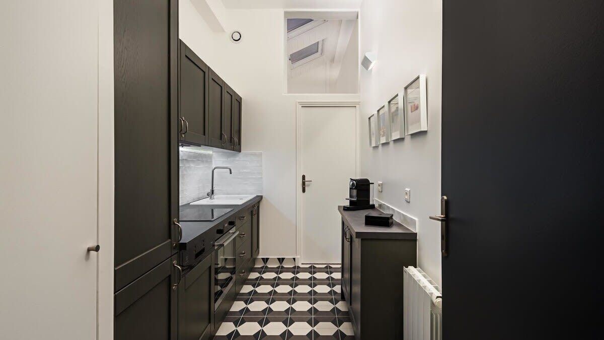 A compact kitchen with dark cabinets, a white countertop, and a black and white tiled floor.