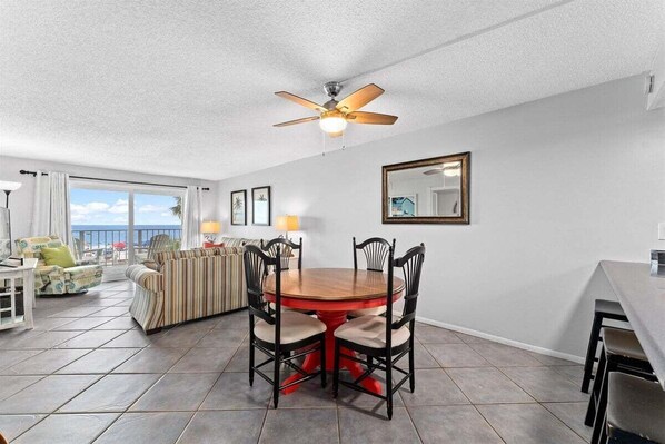 A dining area with a round table and chairs, a ceiling fan, and a large window offering a view.
