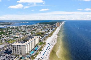 A coastal cityscape with a beachfront hotel featuring multiple buildings, a parking lot, and a beach with umbrellas.