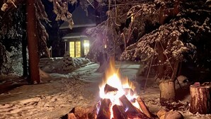 A snow-covered outdoor area with a campfire, trees, and a building in the background. - Secluded Tustin Cabin with Fire Pit and Hiking Trails (Tustin)