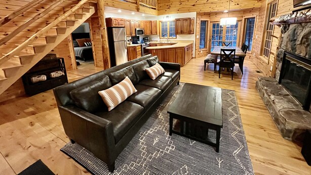 A log cabin interior with a living room, dining area, kitchen, and a staircase leading to an upper level. - Secluded Tustin Cabin with Fire Pit and Hiking Trails (Tustin)