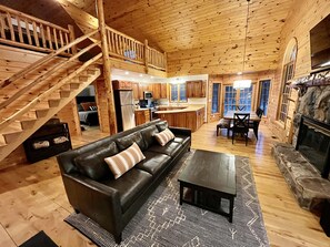 A log cabin interior with a living room, dining area, kitchen, and a staircase leading to an upper level.