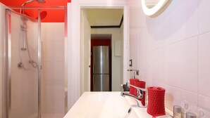 A modern bathroom with a glass-enclosed shower, a white sink with red towels, and toiletries on the counter.