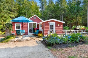 Una cabaña roja con un porche, mobiliario exterior azul y un jardín con diversas plantas y flores.
