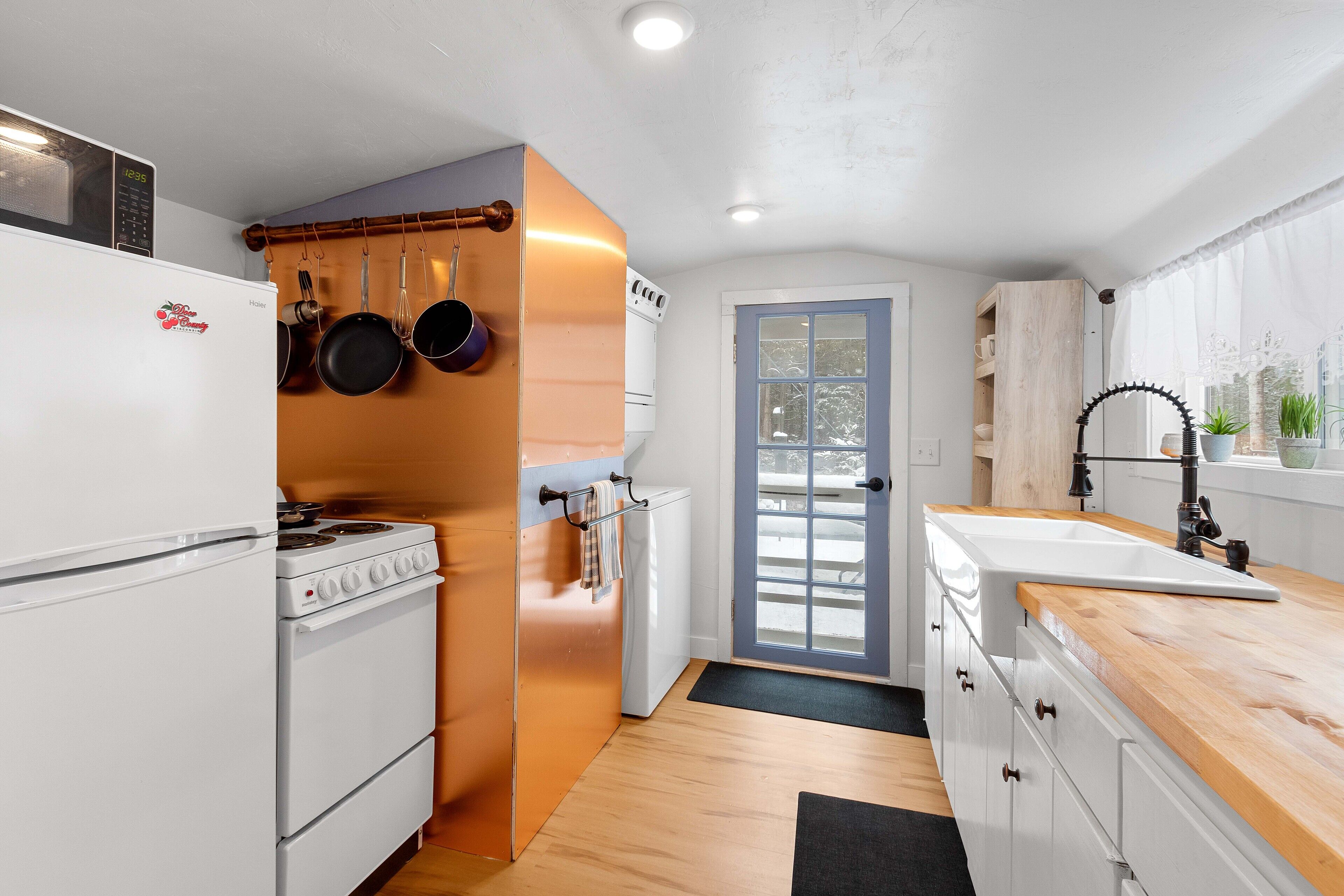 A compact kitchen with a stove, oven, and refrigerator, a wooden countertop, and a sink with a faucet.