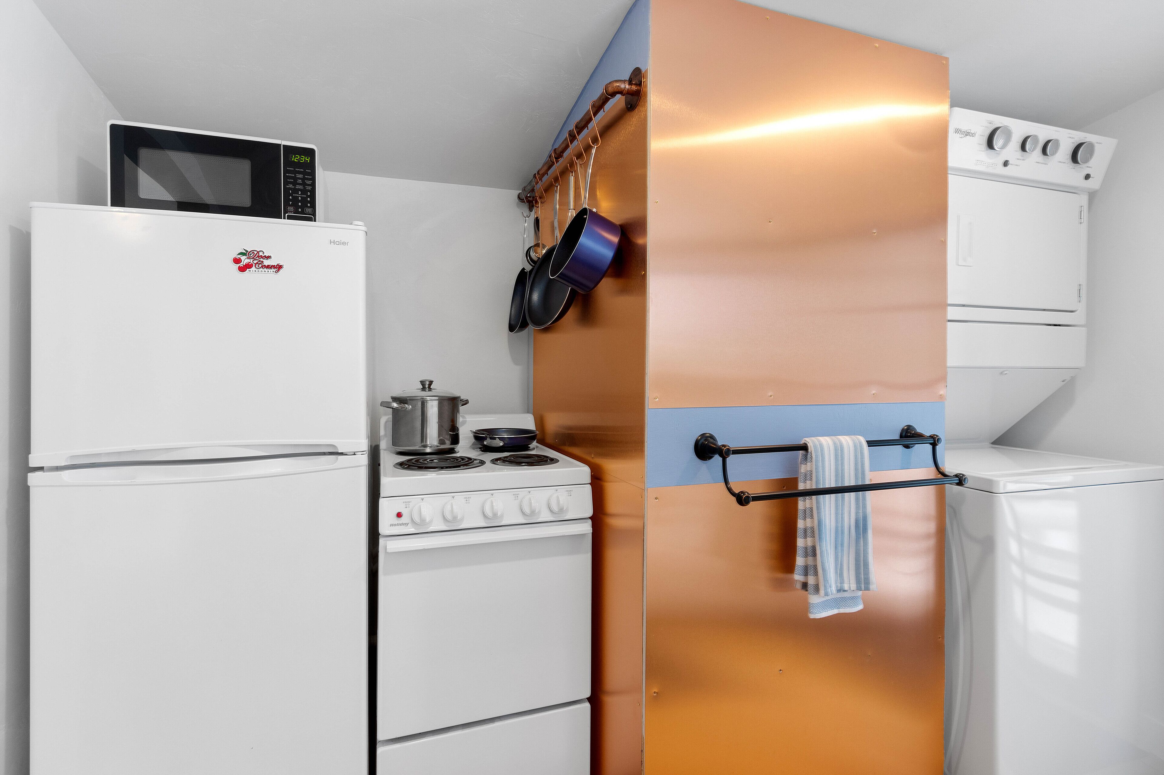 Una kitchenette compacta equipada con refrigerador, microondas, estufa y un colgador para ollas.