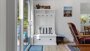 Une pièce avec un banc blanc muni de crochets, une petite table et une chaise.