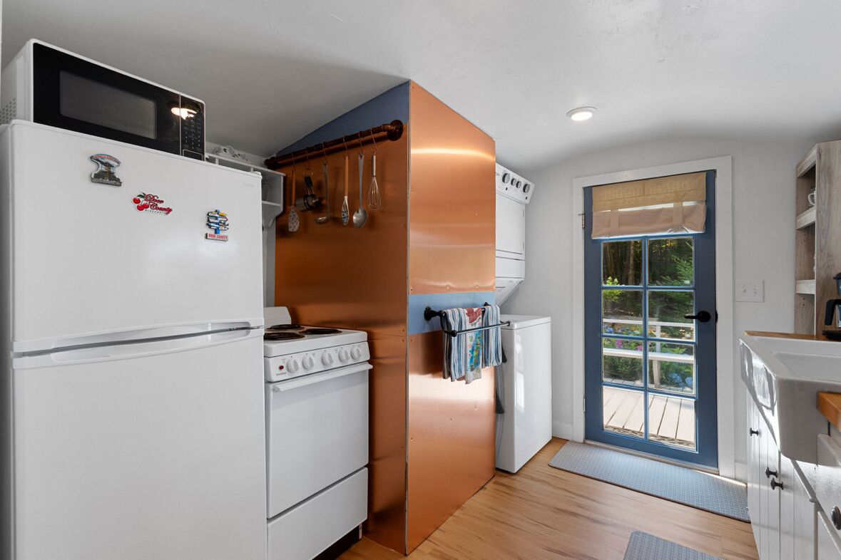 Una cocina compacta con refrigerador, estufa y horno blancos, un extractor de aire color cobre y una puerta que da a un balcón.