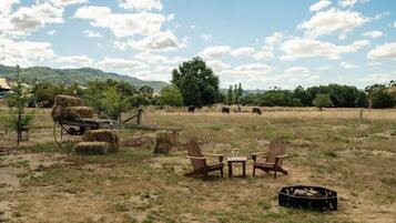 Entorno rural al aire libre con pacas de heno, un carro de madera y un hoyo de fuego.