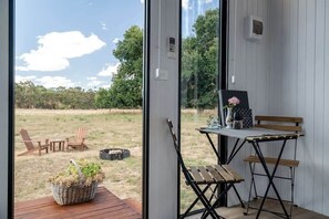 A room with a large window, a wooden deck, a small table with a chair, and a bench. - JBJK Homestead by Tiny Away (Gobur)