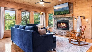 L’intérieur d’un chalet chaleureux, avec une cheminée en pierre, un canapé bleu et un fauteuil à bascule.