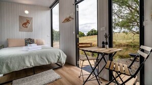 A bedroom with a bed, a wooden table, and a bench. - The Meadows Tiny House by Tiny Away (Macclesfield)