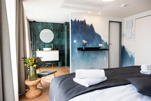 Une chambre d’hôtel moderne, équipée d’un lit, d’une salle de bain avec un grand miroir, d’un lavabo et d’une étagère murale contenant des articles de toilette.