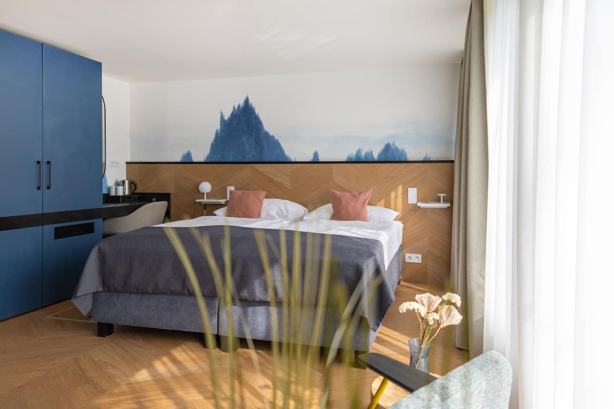 Una habitación de hotel moderna con cama, escritorio y vistas a la montaña.