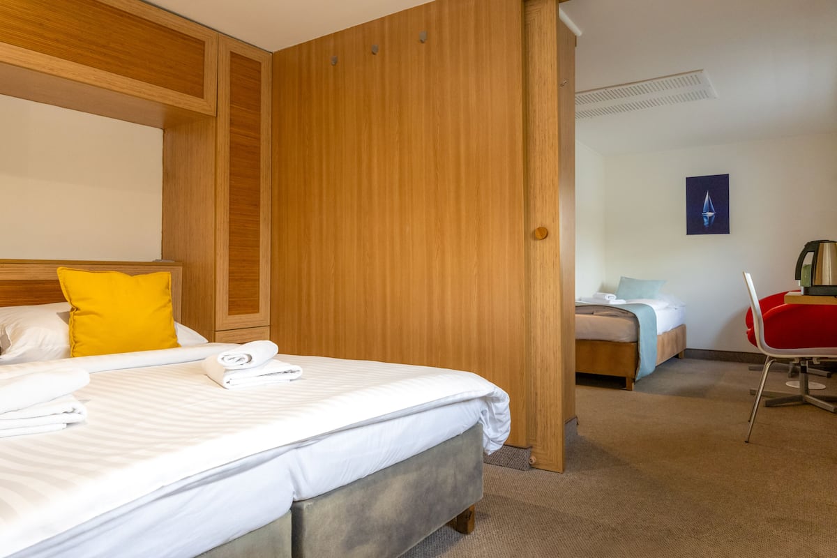 Habitación de hotel con cama, armario de madera, escritorio con silla y una mesita de noche.