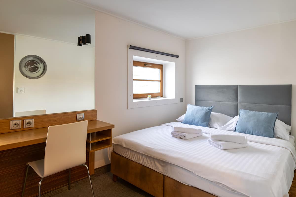 Un dormitorio con cama, escritorio, silla, ventana y lámpara fijada a la pared.