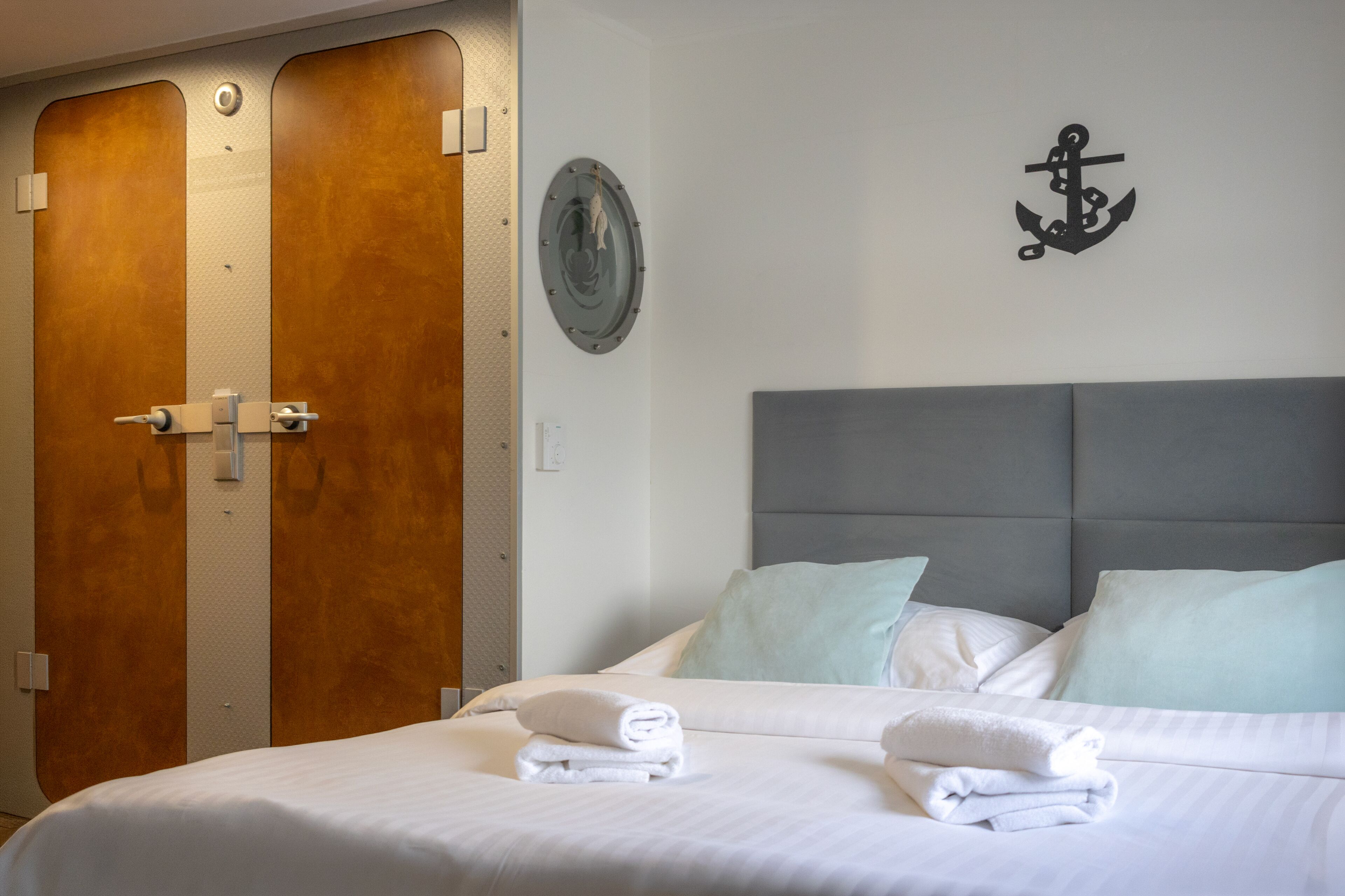A hotel room with a bed, two wooden doors, a wall-mounted circular object, and a black anchor decoration.
