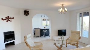 Een moderne woonkamer met een open haard, twee leren fauteuils, een bank en een glazen salontafel, en een televisie.